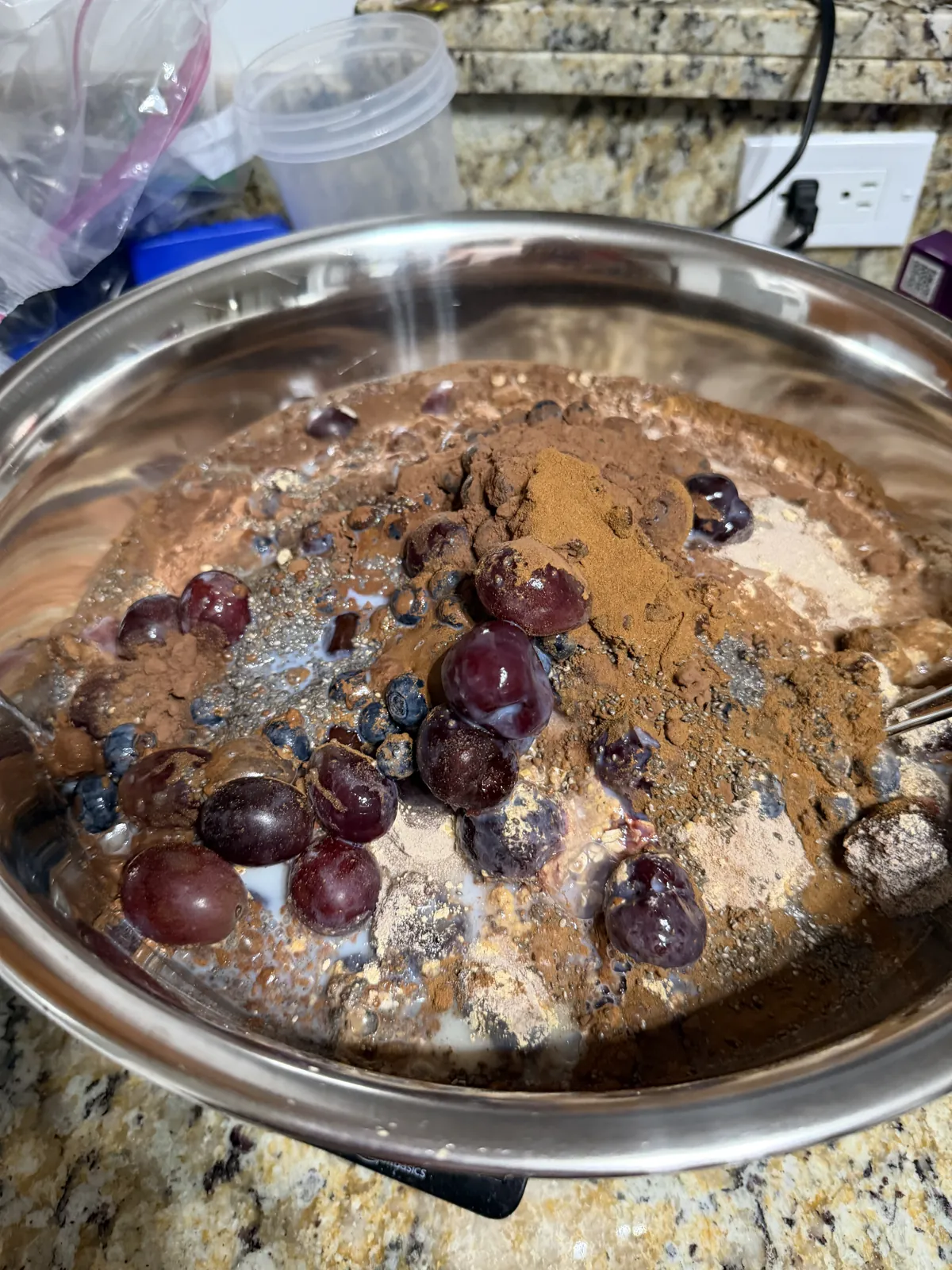Dutch-process cocoa and spice piled over frozen dark cherries, blueberries and milk in a steel mixing bowl, before stirring