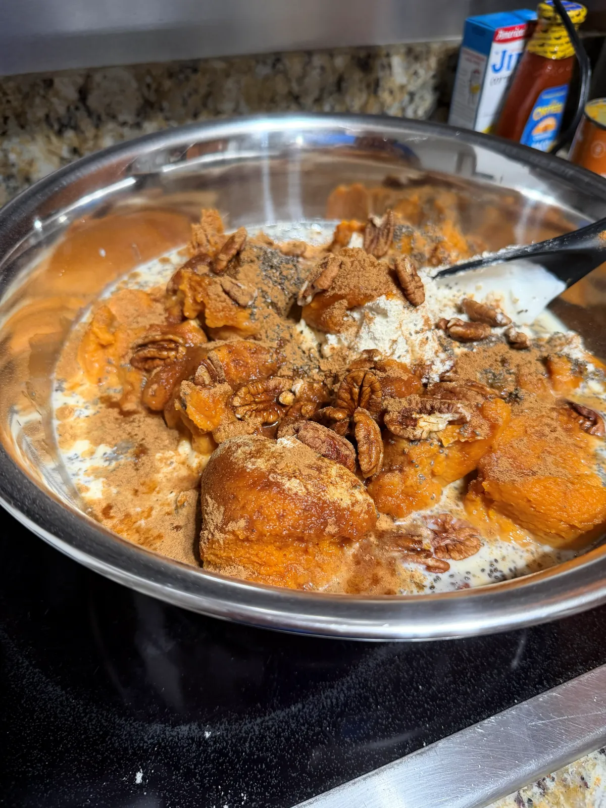 Canned pumpkin purée, pecans and pumpkin pie spice piled on yogurt and oats in a steel mixing bowl, before stirring